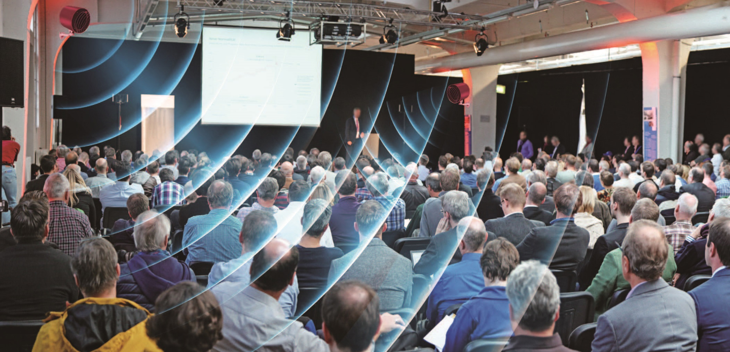Large indoor conference with attendees protected by invisible ViRaTon disinfection waves, demonstrating safe human interaction in crowded environments.